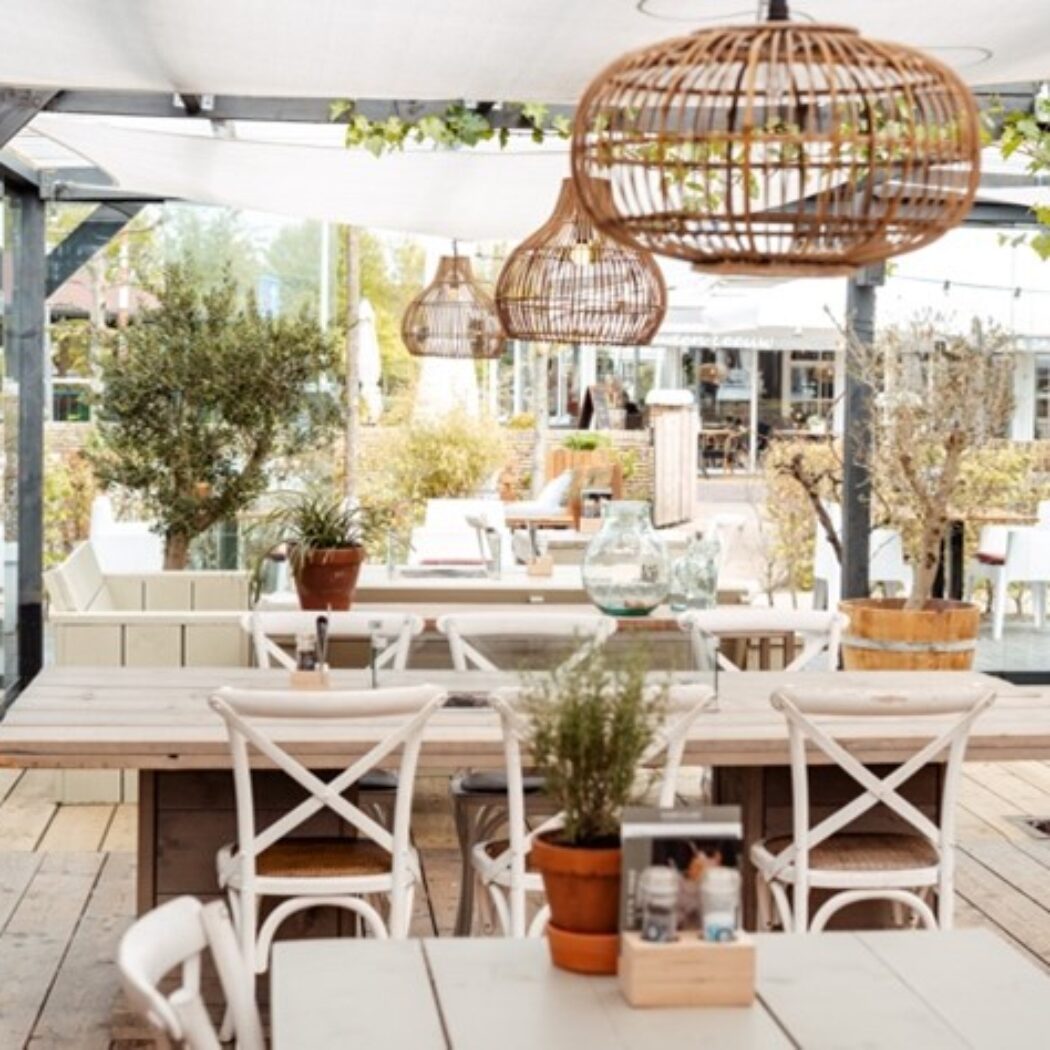 Sfeervol buitenrestaurant met houten meubels, rieten lampen en veel groen.