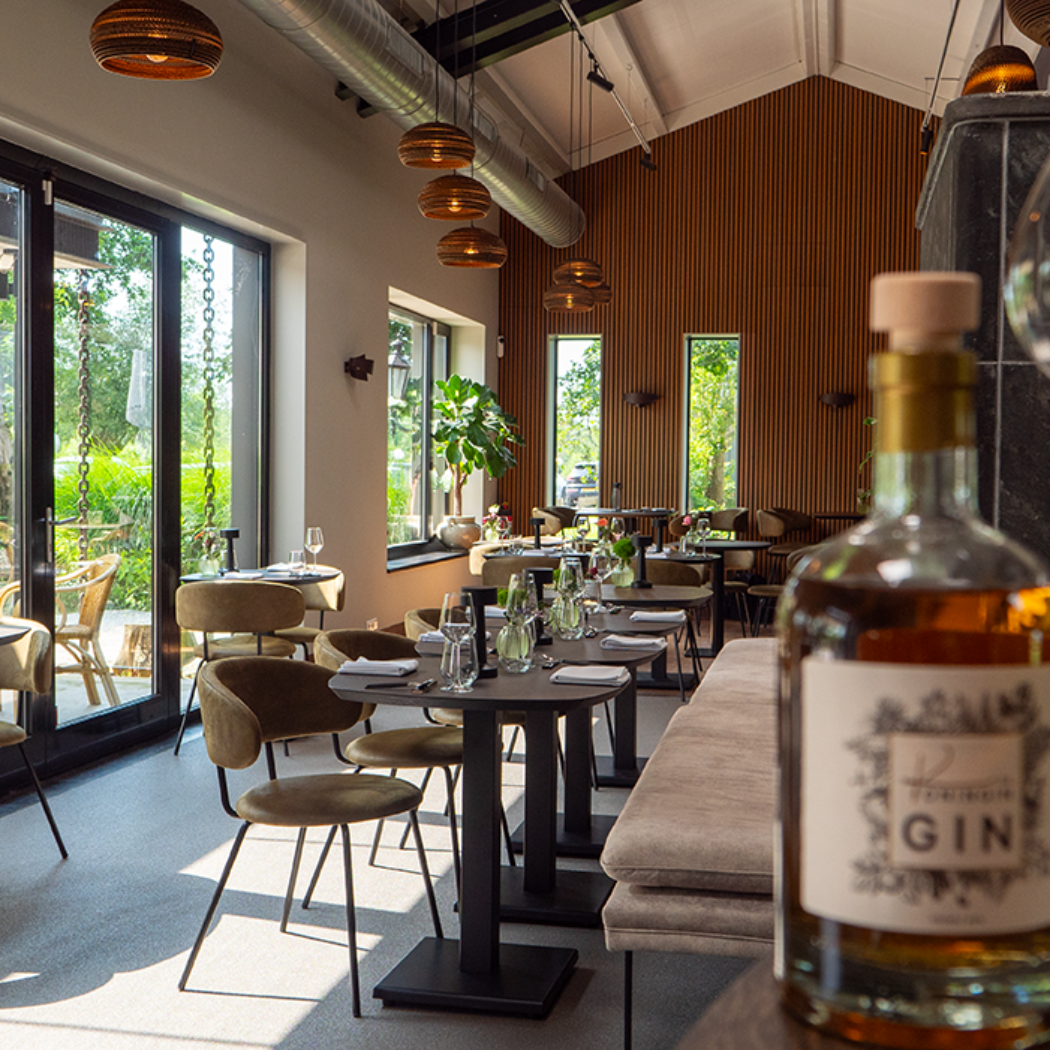 Fles GIN en glas op houten tafel in een modern restaurant met houten muren en uitzicht op groen terras.