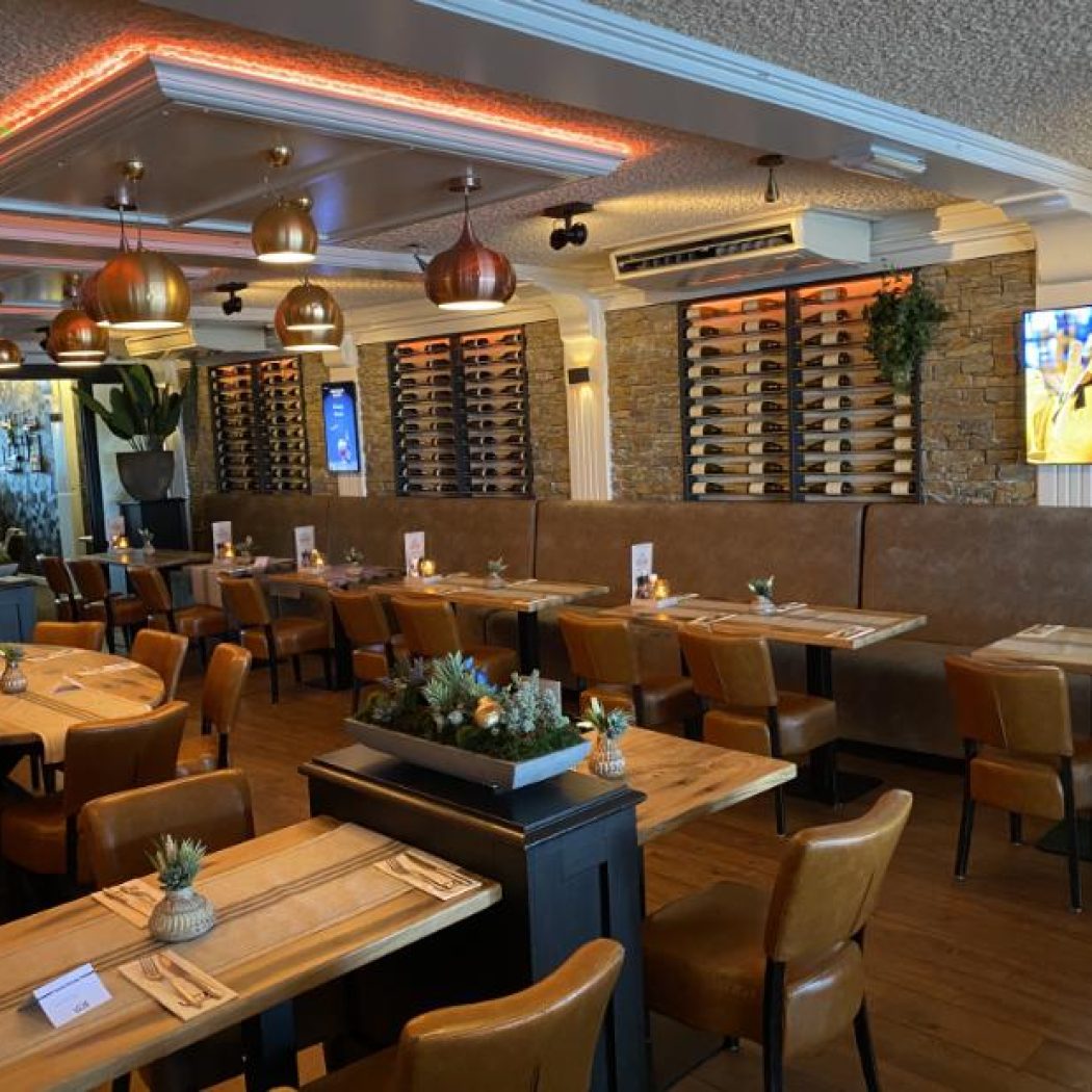 Sfeervol restaurantinterieur met houten tafels, leren stoelen, een lange gestoffeerde bank en wijnrekken aan stenen muren.
