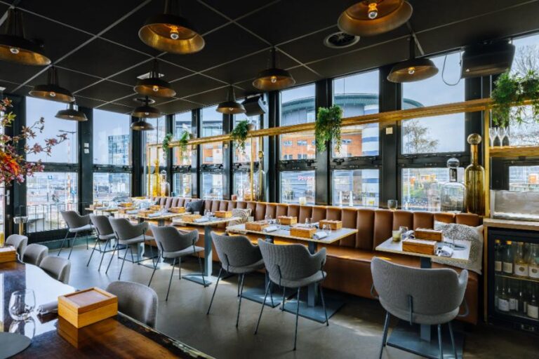 Modern restaurant interieur met bruine banken, grijze stoelen, gouden lampen en uitzicht door grote ramen.