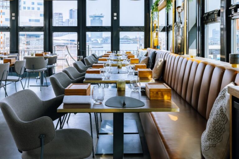 Stijlvol restaurant interieur met bruine banketbank, grijze stoelen en houten tafels; uitzicht op stad en water.