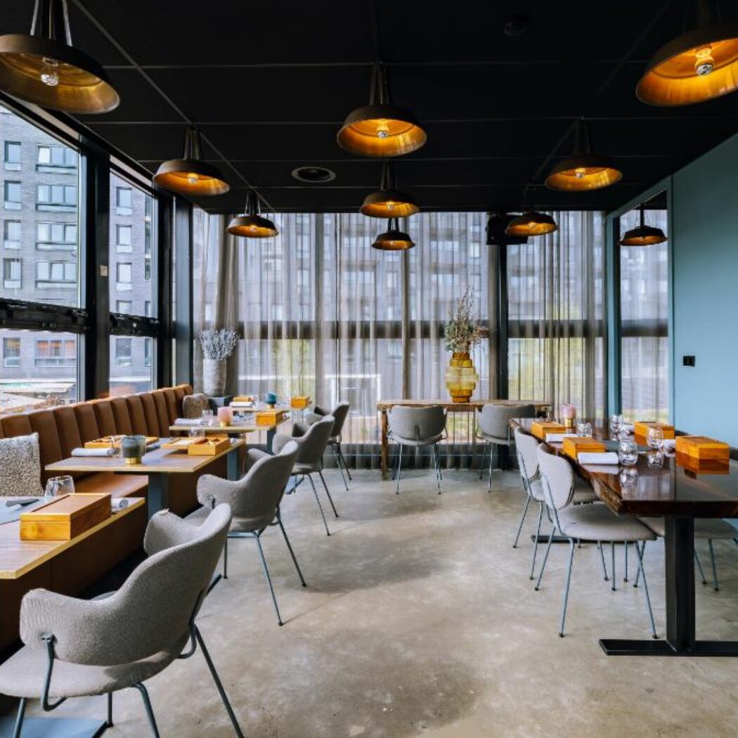 Modern restaurant interieur met bruine leren banken, houten tafels, grijze stoelen, gouden hanglampen en grote ramen.