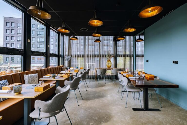 Modern restaurant interieur met bruine leren banken, houten tafels, grijze stoelen, gouden hanglampen en grote ramen.