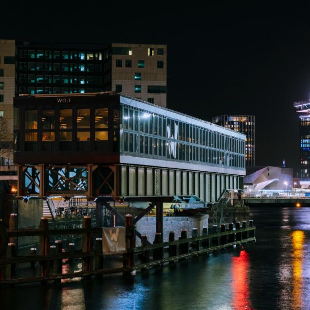 Verlicht WOLF gebouw aan het water in Amsterdam s nachts, met moderne architectuur en reflecties.