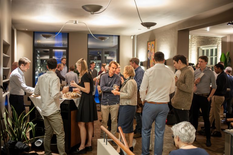 Een groep mensen praat en drinkt tijdens een sfeervolle indoor borrel met hapjes.