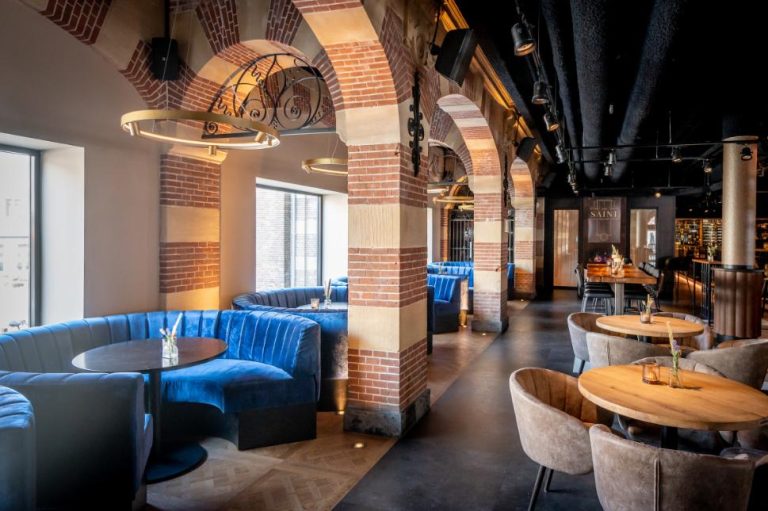 Modern restaurantinterieur SAINT met blauwe fluwelen banquettes, bakstenen bogen en warme verlichting.