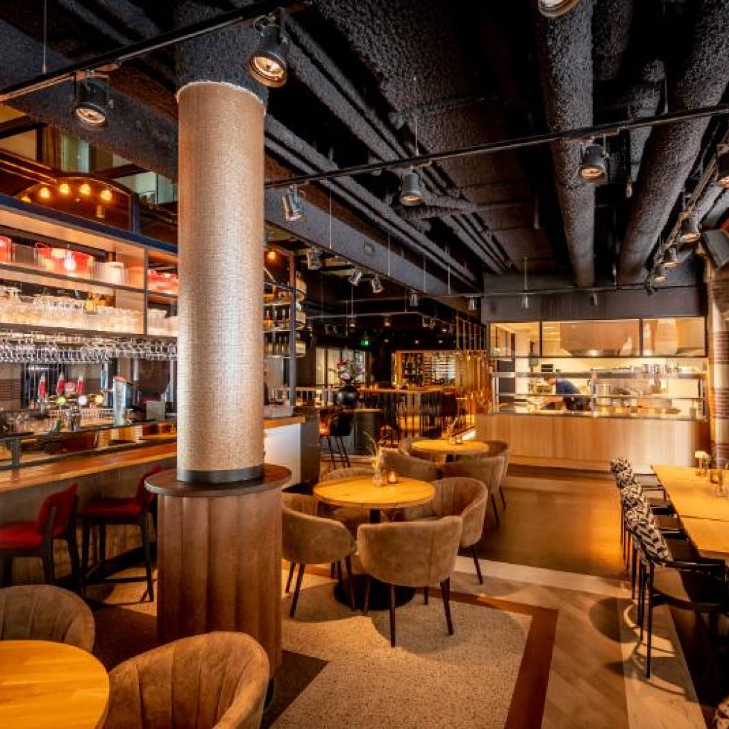 Sfeervol restaurant interieur met bar, comfortabele zitjes, open keuken en decoratieve bakstenen bogen.