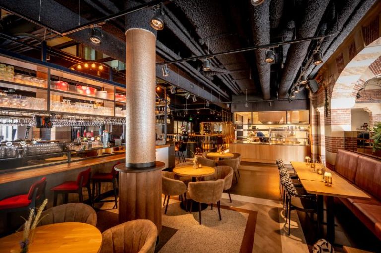 Sfeervol restaurant interieur met bar, comfortabele zitjes, open keuken en decoratieve bakstenen bogen.