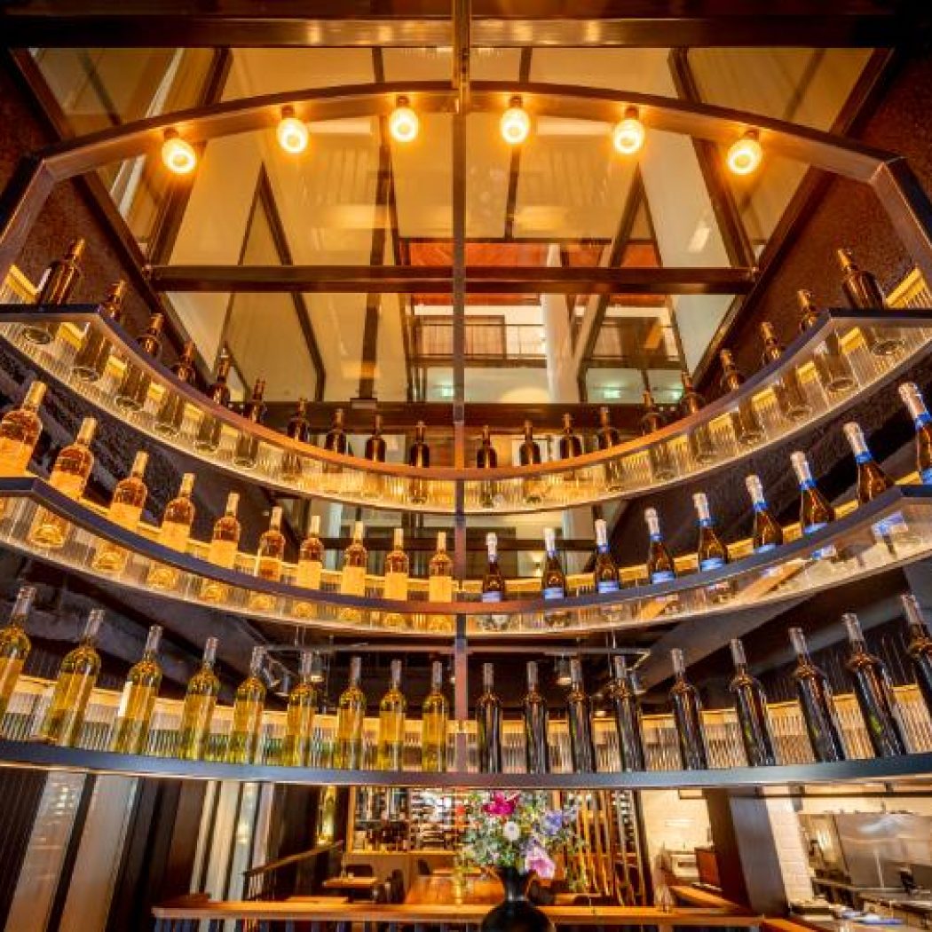 Groot, gebogen wijnrek met veel verlichte flessen in een moderne restaurantomgeving.