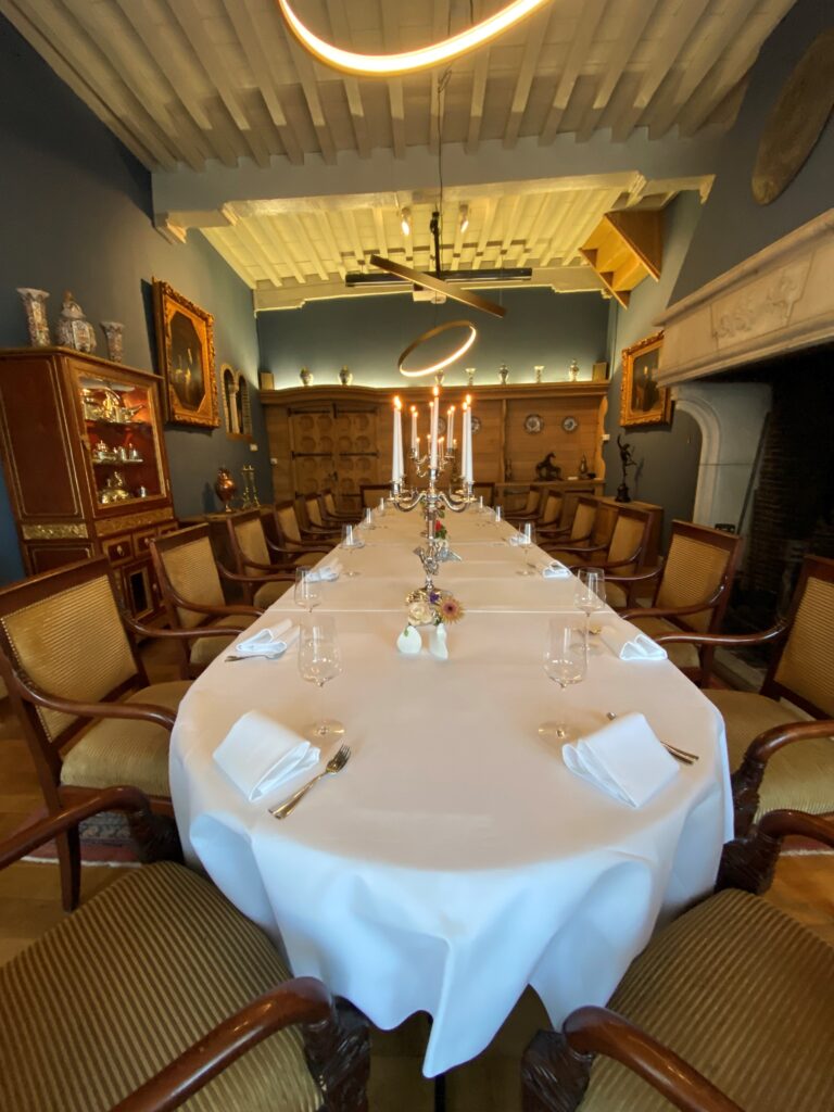 Formele eetzaal met lange gedekte tafel, zilveren kandelaars, houten stoelen en moderne verlichting aan het balkenplafond.