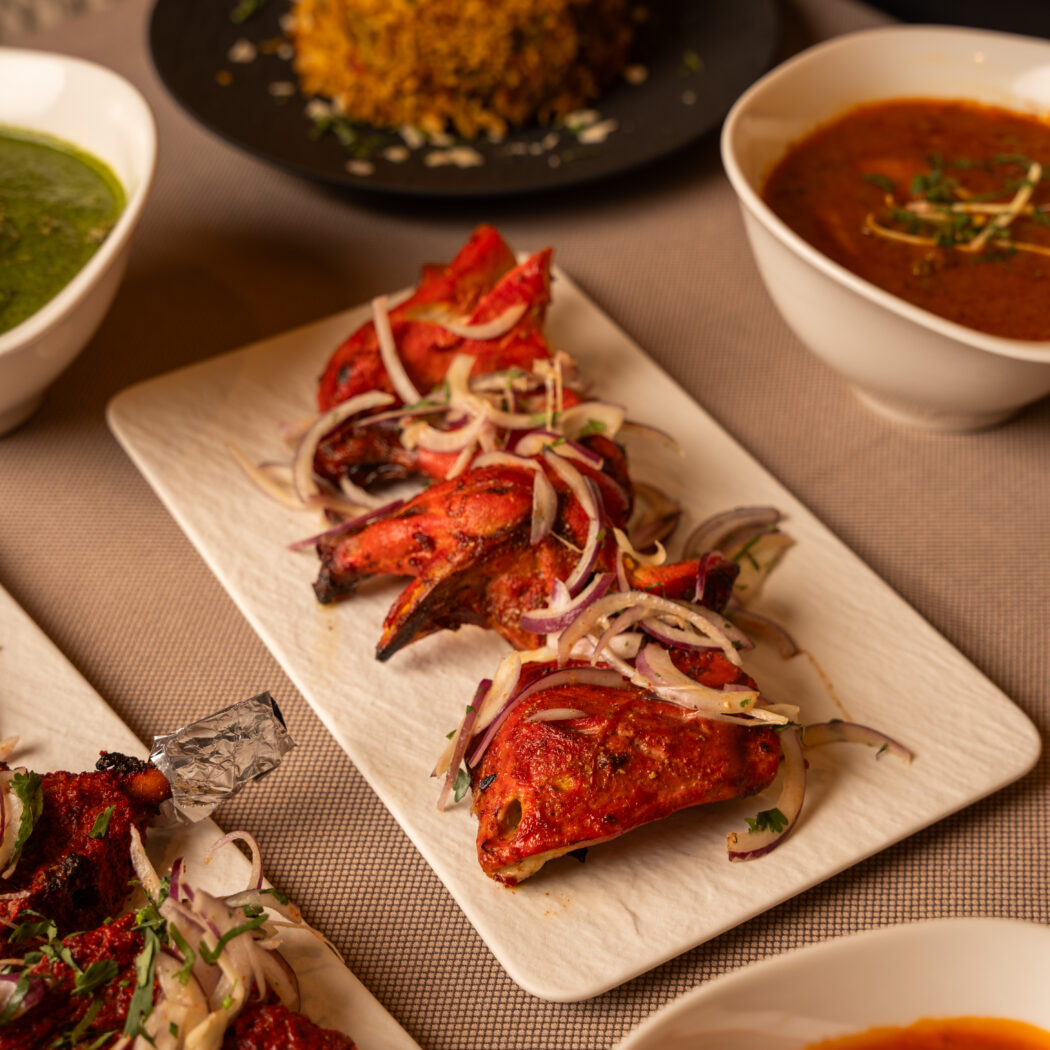 Gegrilde rode Tandoori kipstukken met ringen rode ui en koriander, omringd door Indiase bijgerechten.
