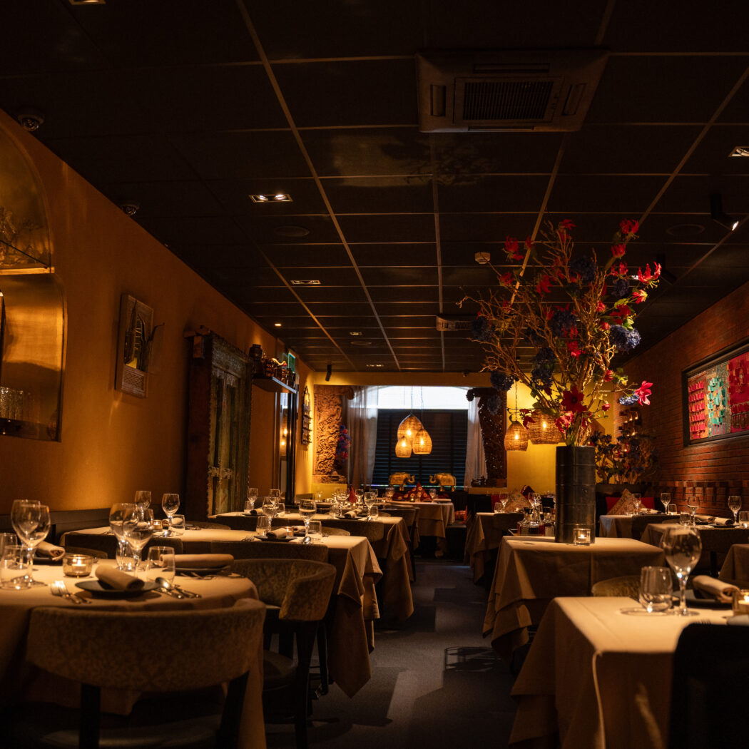 Gedekte tafels in een sfeervol restaurant met warme verlichting, een spiegelboog en kleurrijke wanddecoraties.