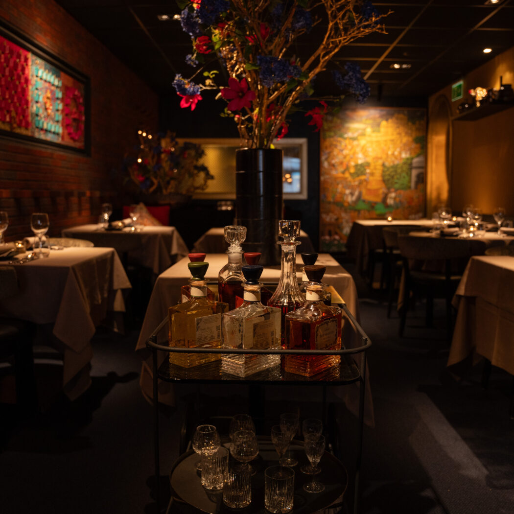 Sfeervol donker restaurant met gedekte tafels, kleurrijke kunst aan de bakstenen muur en een drankentrolley in de voorgrond.