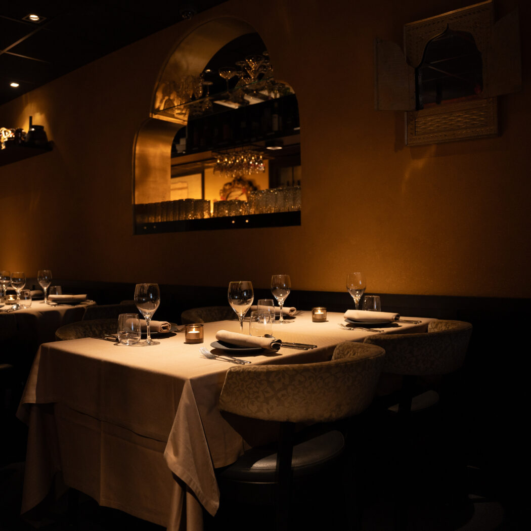 Sfeervol restaurant met gedekte tafels, comfortabele stoelen en warme verlichting, inclusief een bar achter een boog.