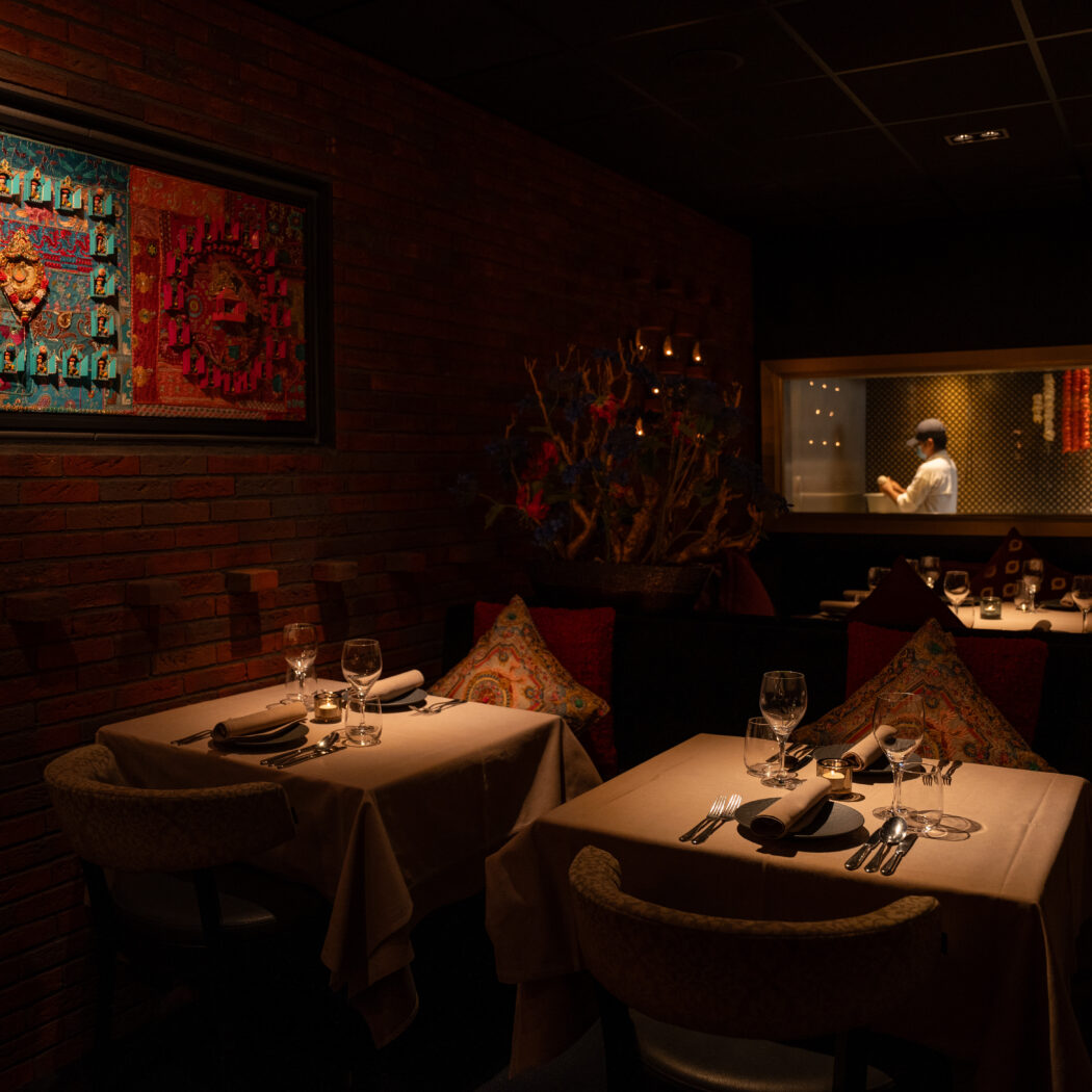 Sfeervol restaurant met gedekte tafels, een bakstenen muur, groot Aziatisch kunstwerk en een chef in de open keuken.