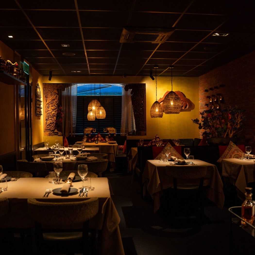 Sfeervol restaurantinterieur met gedekte tafels, warme verlichting, bakstenen muur en rieten hanglampen.