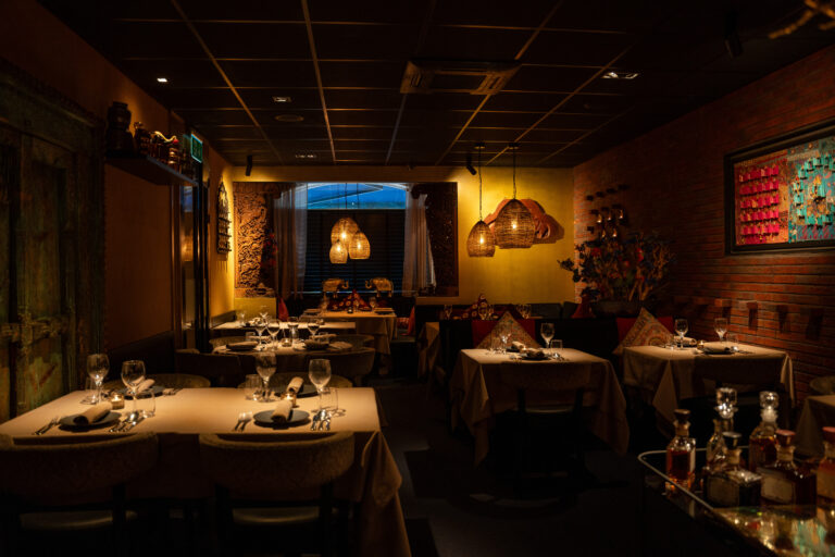 Sfeervol restaurantinterieur met gedekte tafels, warme verlichting, bakstenen muur en rieten hanglampen.