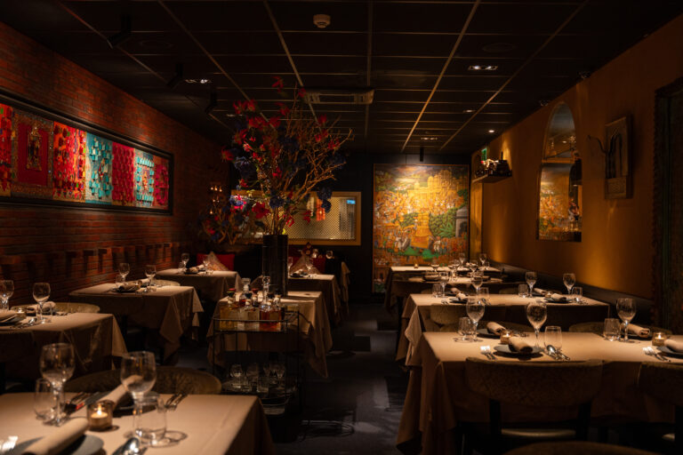 Sfeervol restaurantinterieur met gedekte tafels, bakstenen muur, oosterse kunst en grote bloemdecoratie.