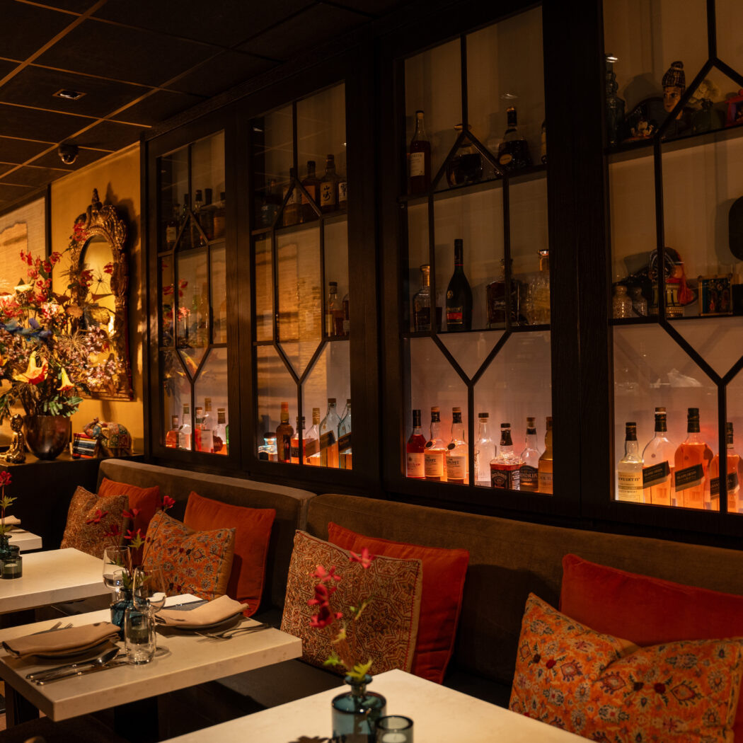 Gezellig restaurant interieur met gedekte tafels, rode kussens en verlichte drankenkasten.