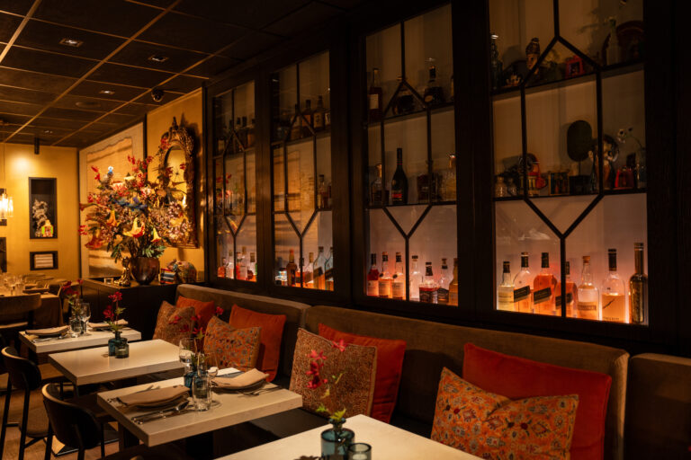 Gezellig restaurant interieur met gedekte tafels, rode kussens en verlichte drankenkasten.