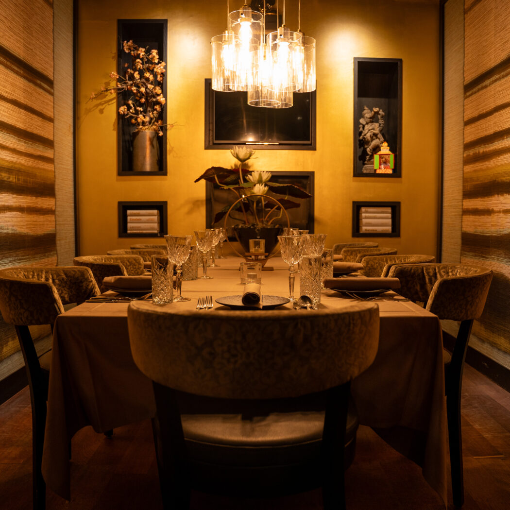 Gezellig verlichte, luxe eetzaal met lange gedekte tafel, pluche stoelen en gouden muren.