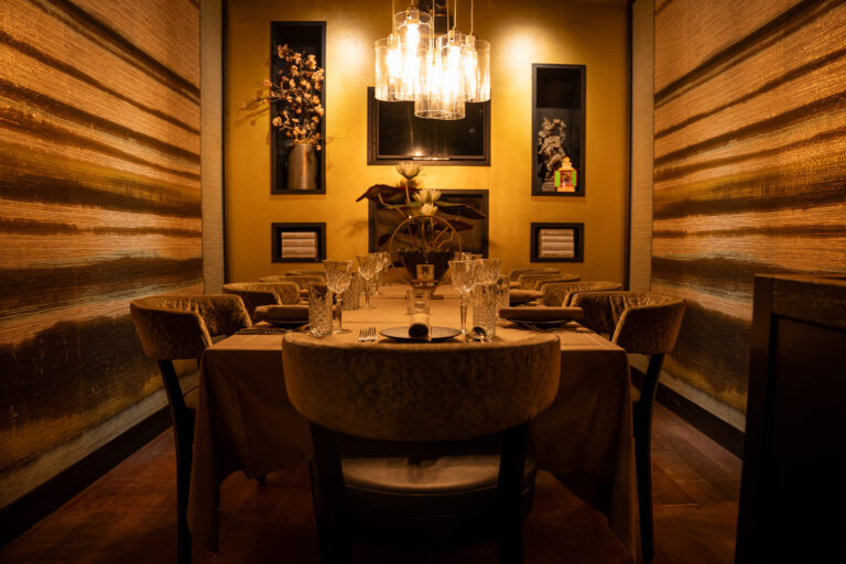 Gezellig verlichte, luxe eetzaal met lange gedekte tafel, pluche stoelen en gouden muren.