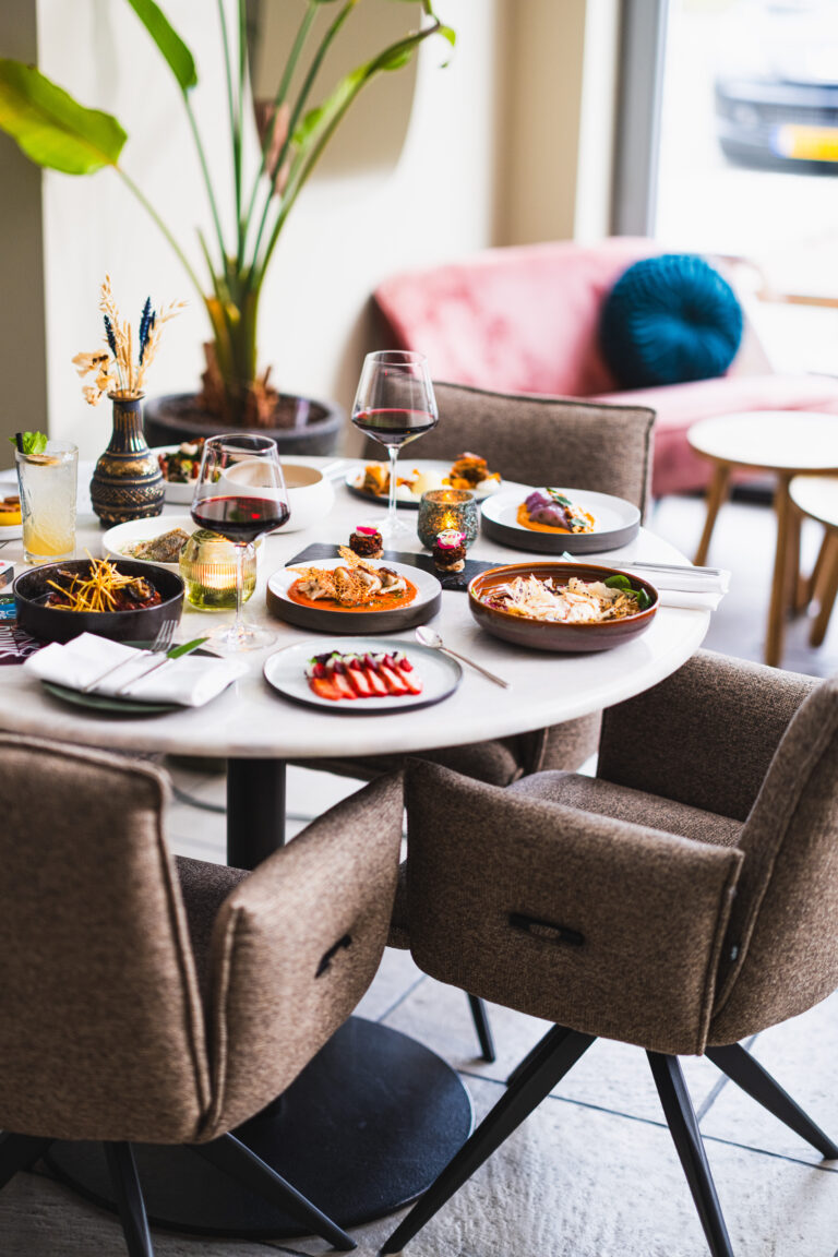 Ronde witte tafel met diverse kleine gerechten, wijnglazen en een cocktail in een sfeervol restaurant.