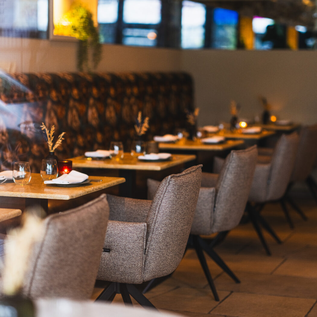 Sfeervolle restaurant eetzaal met rijen grijs gestoffeerde stoelen, opgedekte tafels en kaarslicht.
