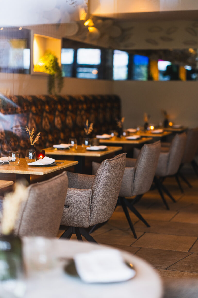 Sfeervolle restaurant eetzaal met rijen grijs gestoffeerde stoelen, opgedekte tafels en kaarslicht.