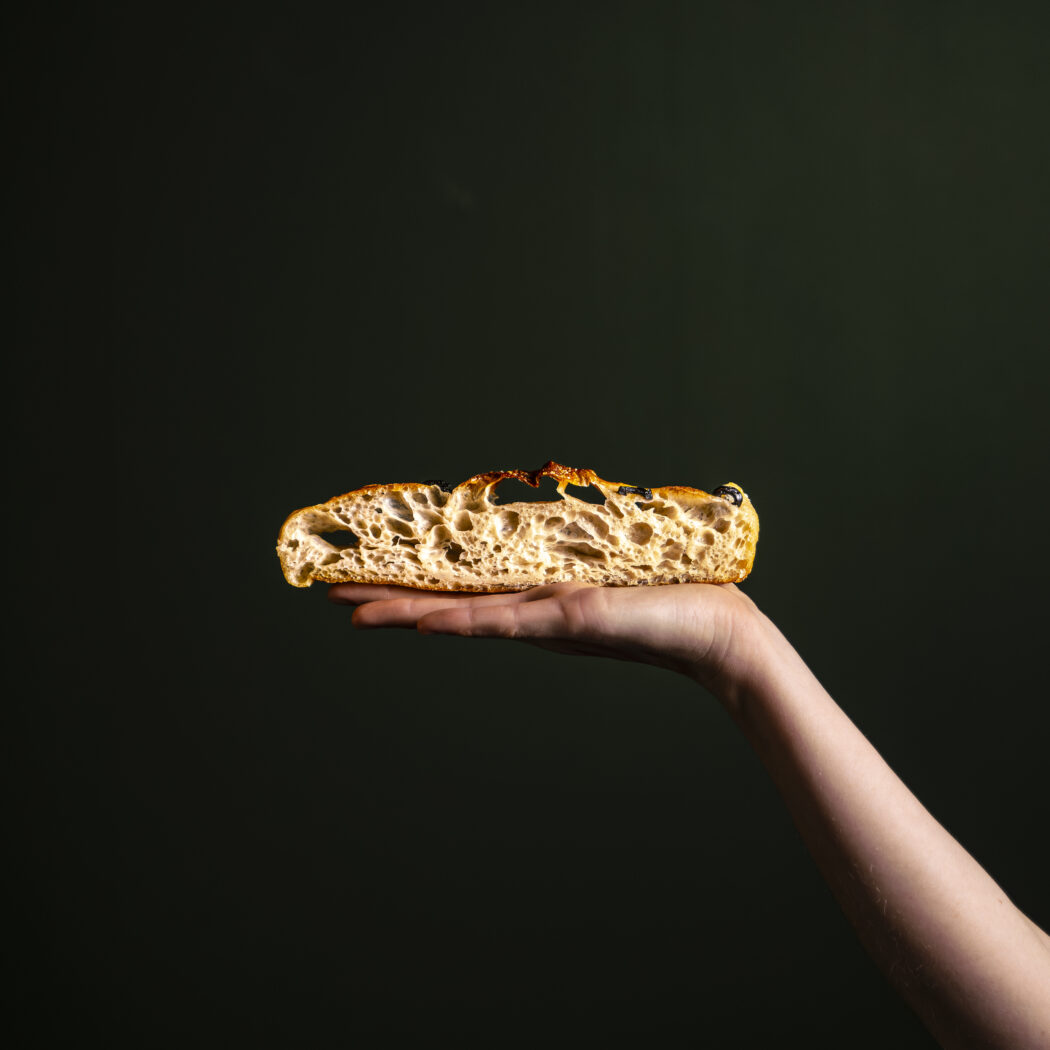Een lichte hand houdt een doorgesneden, goudbruine snede ambachtelijk brood vast.
