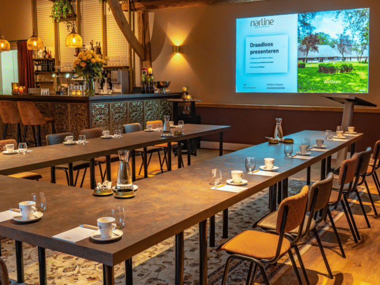 Sfeervolle vergaderzaal met U-vormige tafels, presentatiescherm Draadloos presenteren en bar op de achtergrond.