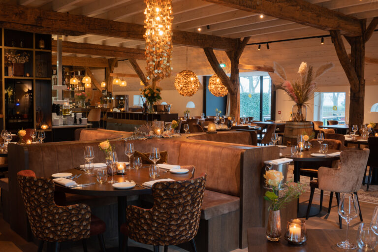 Sfeervol restaurant interieur met houten balken, comfortabele zitbanken, gedekte tafels en warme verlichting.