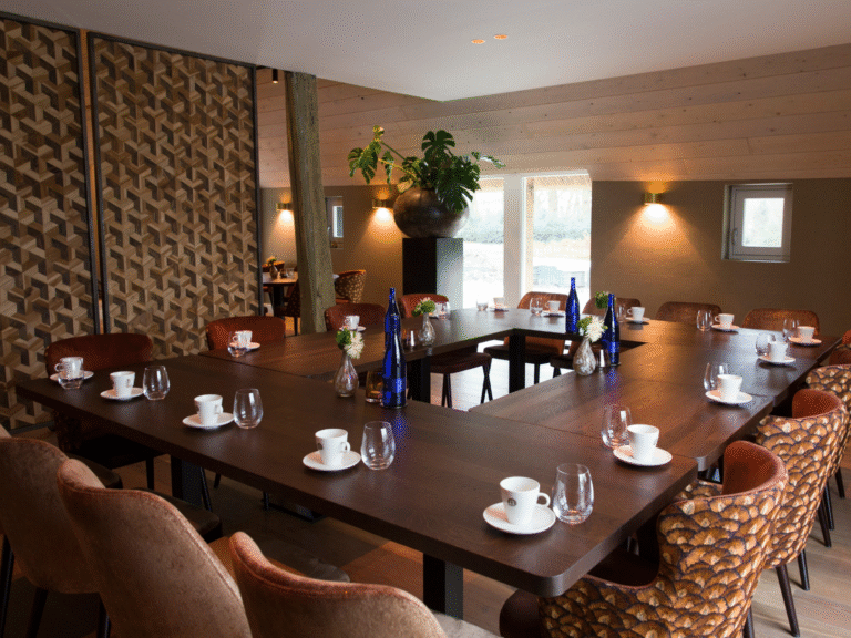 Ruime vergaderzaal met U-vormige houten tafel, luxe stoelen en klaargezette koffie- en waterfaciliteiten.