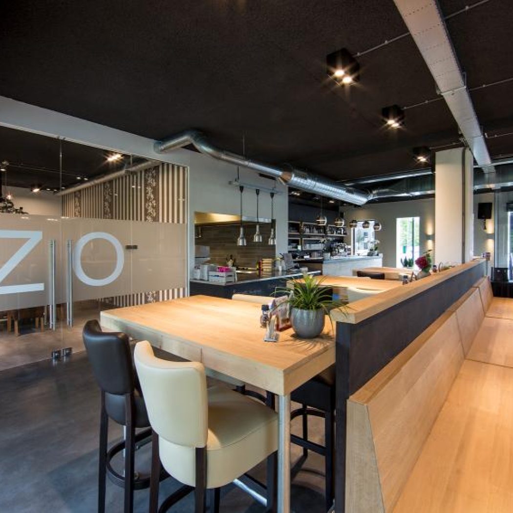 Stijlvol restaurant met hoge houten tafels, lange houten zitbanken en een glazen wand met ZIO.