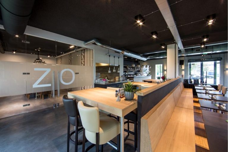 Stijlvol restaurant met hoge houten tafels, lange houten zitbanken en een glazen wand met ZIO.