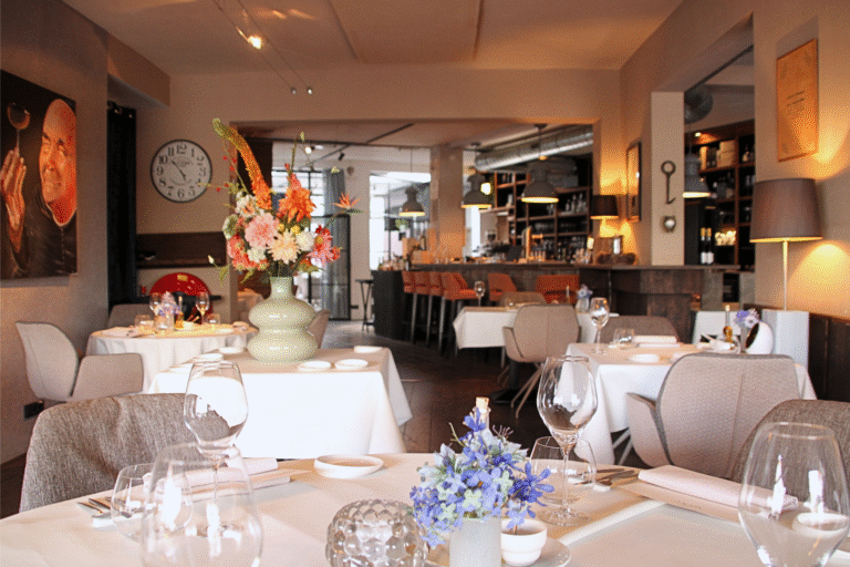 Sfeervol restaurant met gedekte tafels, kleurrijke bloemstukken en een bar met oranje stoelen.