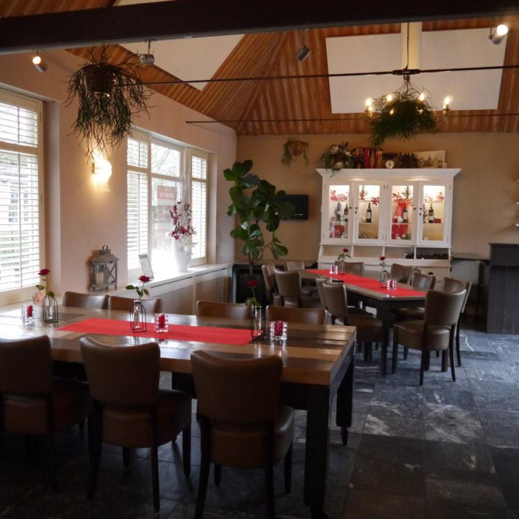 Sfeervolle eetzaal met lange houten tafels, rode lopers, bruine stoelen, witte luiken en bar.
