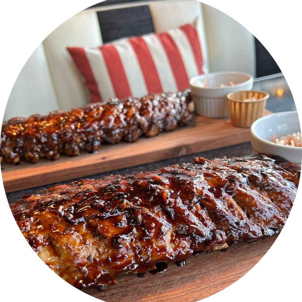 Twee royale porties glanzende spareribs met barbecuesaus op houten planken, met bijgerechten.