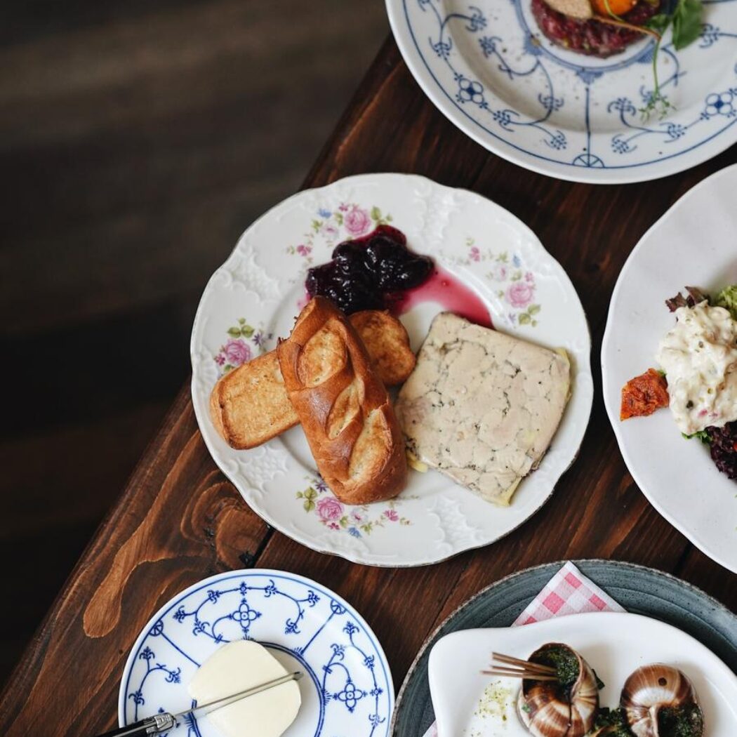 Een houten restauranttafel gedekt met diverse culinaire voorgerechten, waaronder escargots, paté en steak tartare.