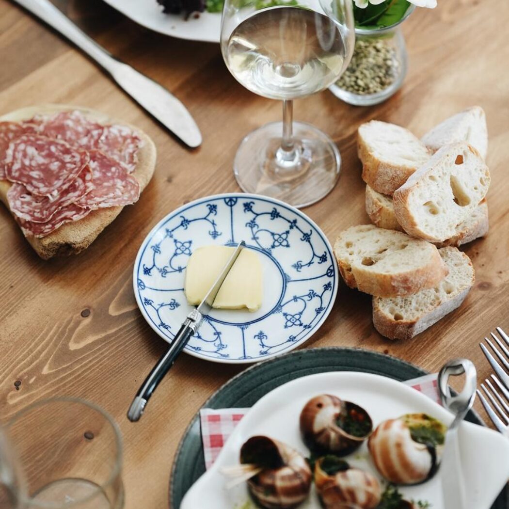 Divers feestelijk diner op houten tafel: escargots, kroketten met salade, brood, salami en witte wijn.