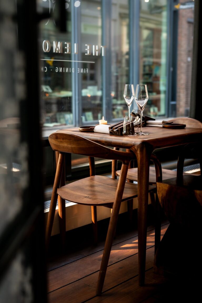 Houten restauranttafel gedekt voor twee met champagneglazen en een brandende kaars, bij raam met Fine Dining reflectie.