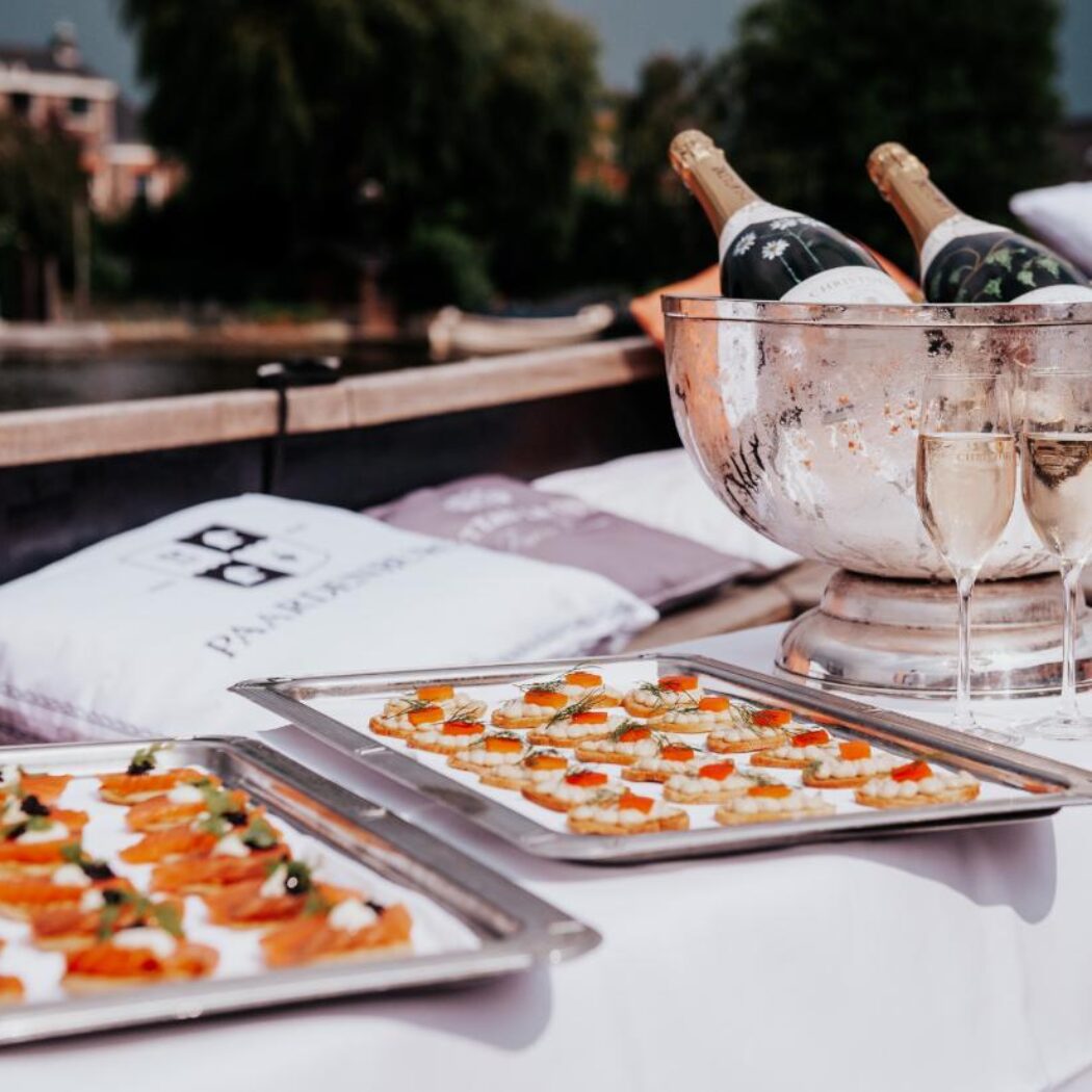 Zalm- en viseitjes-canapés op trays, met twee glazen en champagne in een zilveren koeler op een boot.