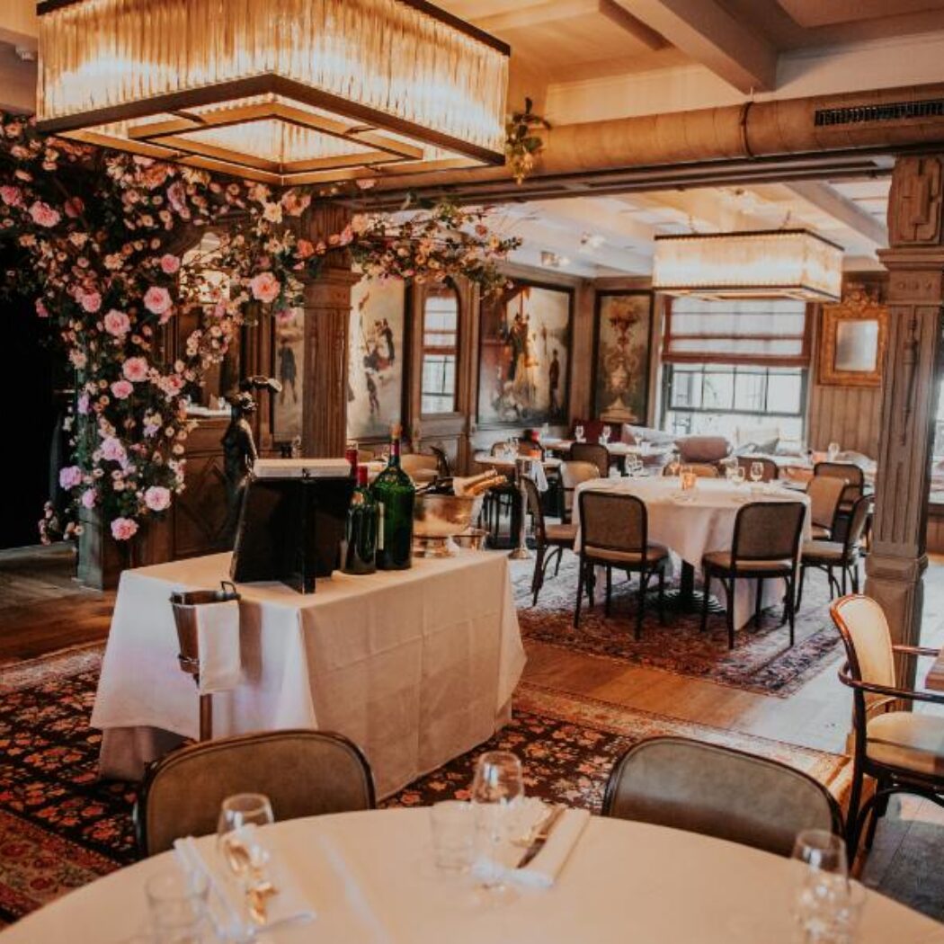 Sfeervolle restaurantzaal met gedekte tafels, weelderige roze bloemdecoraties en glimmende kroonluchters.