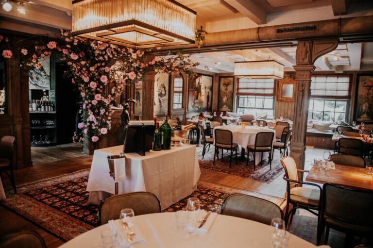 Sfeervolle restaurantzaal met gedekte tafels, weelderige roze bloemdecoraties en glimmende kroonluchters.
