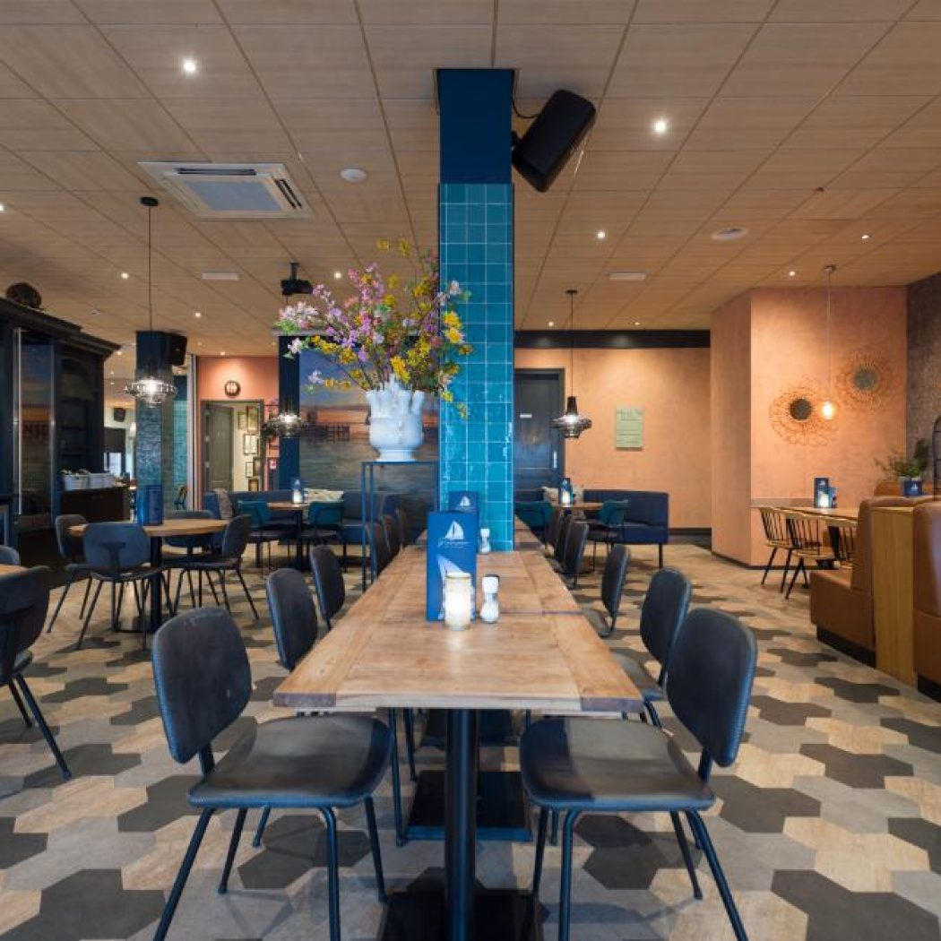 Licht en modern restaurantinterieur met houten tafels, bruine zitbanken, een bar en een hexagonale vloer.
