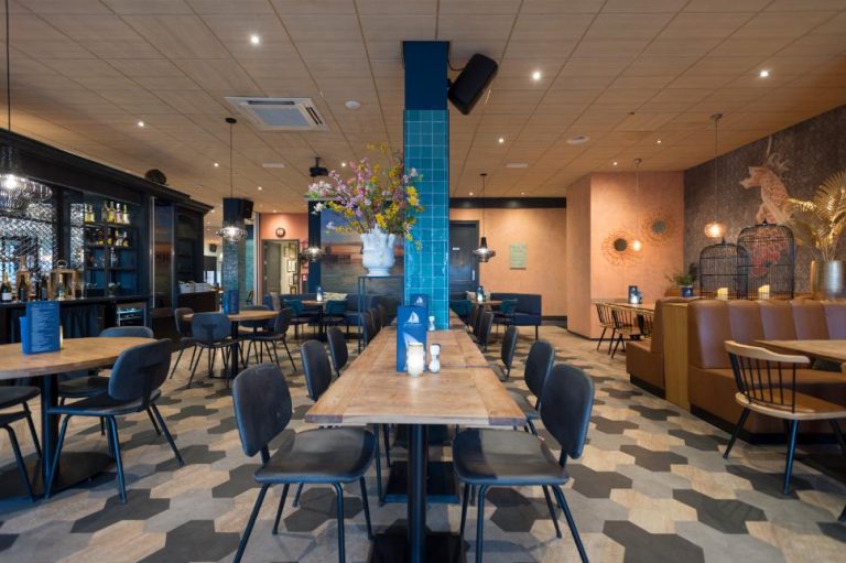Licht en modern restaurantinterieur met houten tafels, bruine zitbanken, een bar en een hexagonale vloer.