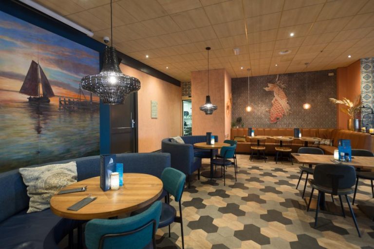Stijlvol restaurant met blauwe en bruine banken, houten tafels, muurschilderingen van een zeilboot en koi, en zeshoekige vloer.