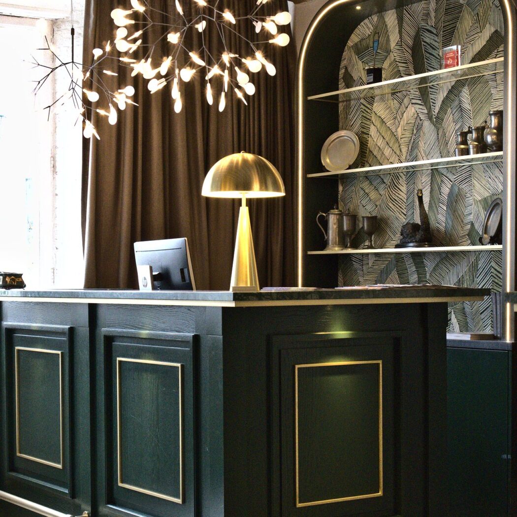 Elegante donkergroene balie met gouden accenten, een HP-monitor en bladvormige kroonluchter.