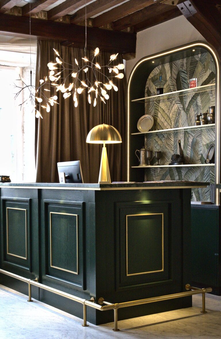 Elegante donkergroene balie met gouden accenten, een HP-monitor en bladvormige kroonluchter.