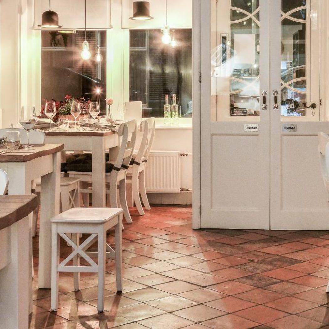 Gezellig restaurantinterieur met gedekte houten tafels, witte stoelen en een tegelvloer, klaar voor gasten.